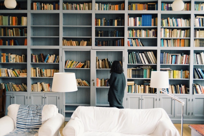 A women stands in front of a bookshelf that rises to the ceiling