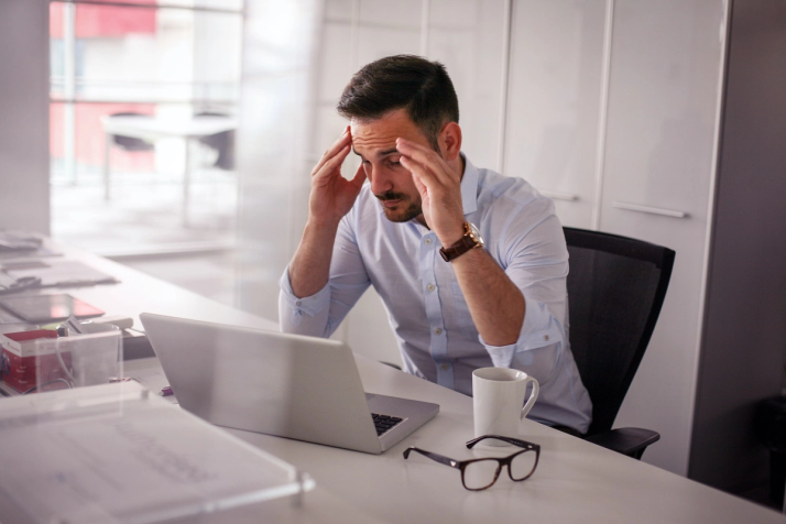 A man sits at a laptop on his desk feeling stressed while dealing with a poorly-designed chatbot