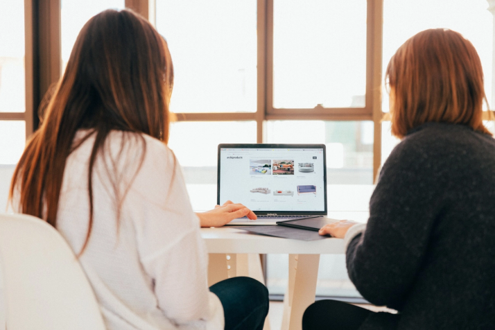 Two women sit at a computer visiting a website that uses a chatbot to help meet their needs